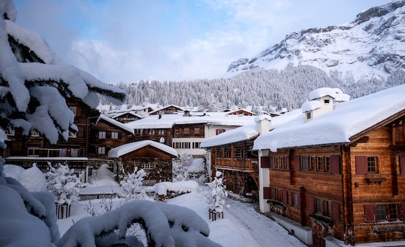 snow covered houses under snowy mountains and snow-covered trees